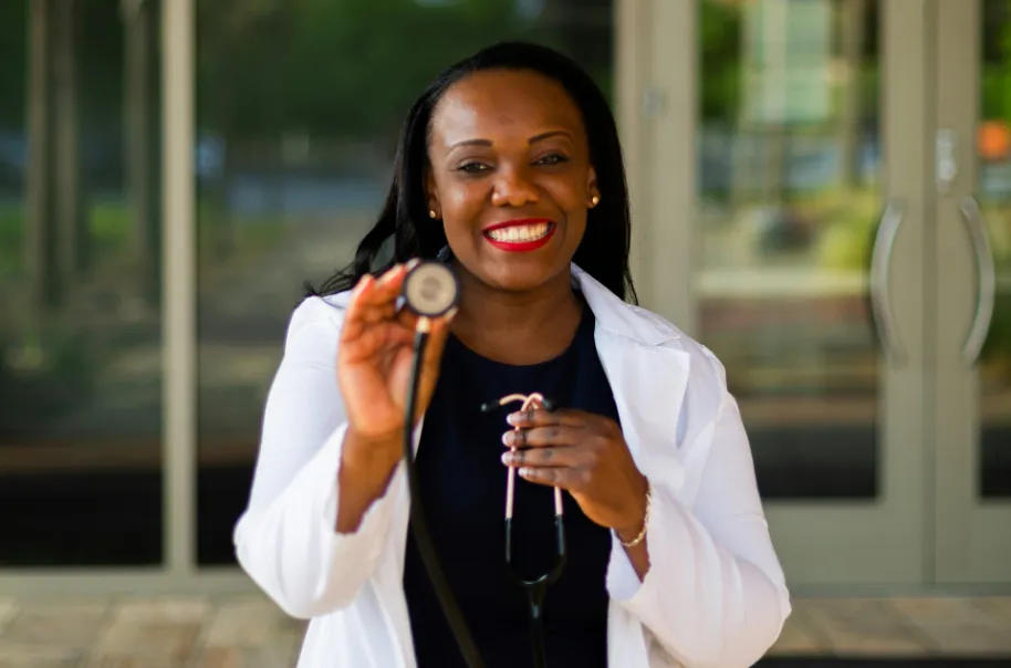 A female doctor smiling while holding up stethoscope